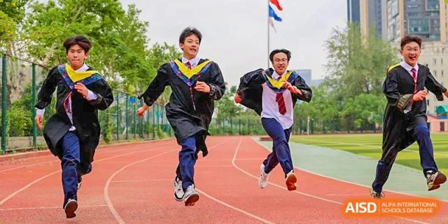 Two students from Henan Zhengzhou Jianye International School running on a red track while wearing their graduation gowns.