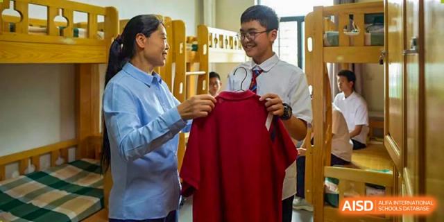 A teacher from Henan Zhengzhou Jianye International School handing a red school jacket to a male staff member.