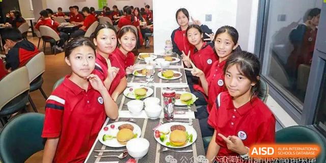 Female students from Henan Zhengzhou Jianye International School in red tops seated together at a table, eating a meal in a school dining area.