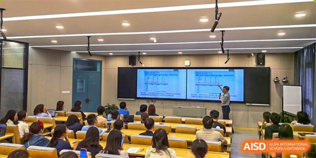 Students from International Department of Jinling High School Hexi Campus seated in a lecture hall attending a class, with an instructor and presentation screens visible.