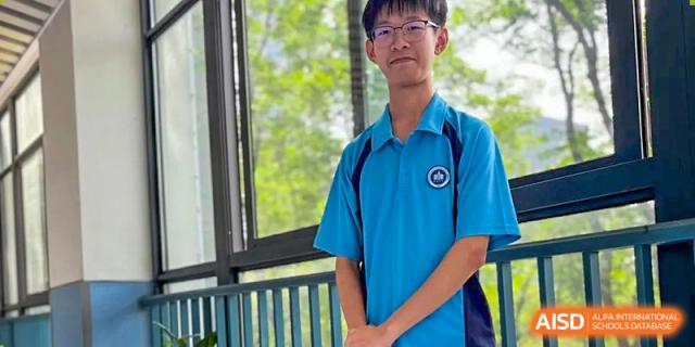 A male student from International Department of Jinling High School Hexi Campus wearing a blue and white school uniform, posing for a portrait outdoors.