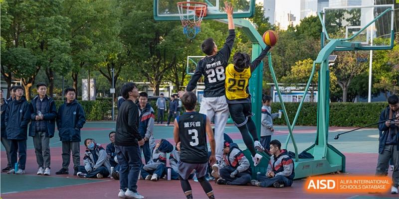Students from International Department of Jinling High School Hexi Campus playing an outdoor basketball game, with one student jumping up for a shot.