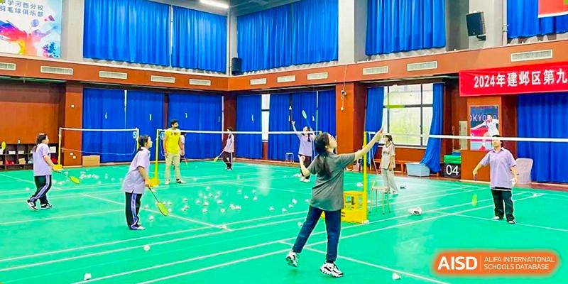 Students from International Department of Jinling High School Hexi Campus practicing or playing badminton in an indoor gymnasium.