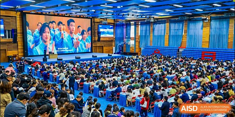 A large audience, likely students and parents of the International Department of Jinling High School Hexi Campus, seated in a bright auditorium for an event.
