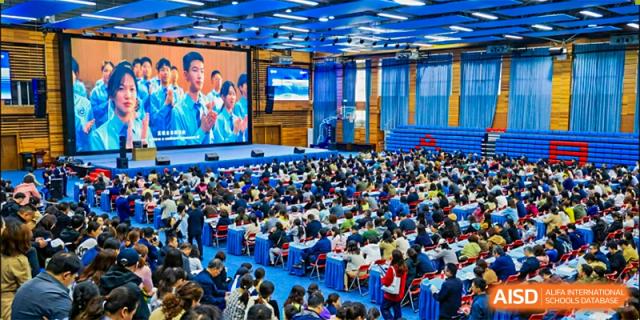 A large audience, likely students and parents of the International Department of Jinling High School Hexi Campus, seated in a bright auditorium for an event.