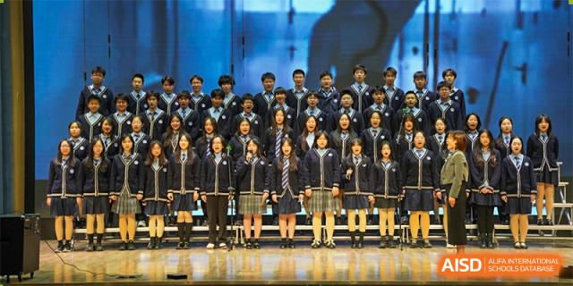 A large group of students from International Department of Jinling High School Hexi Campus dressed in school uniforms posing for a photo on a stage.