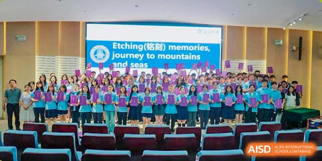 A large group of students from International Department of Jinling High School Hexi Campus posing together in an auditorium, with a banner above reading "Etching (铭刻) memories, journey to mountains and seas."