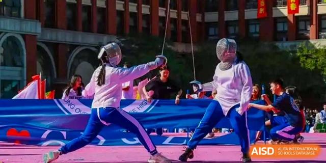 Students from the Guangdong Overseas Chinese High School International Curriculum engaging in a fencing match or demonstration, wearing protective gear and holding foils.
