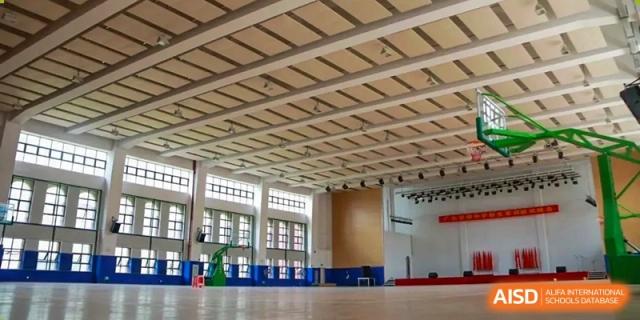 A large, well-lit indoor gymnasium or multipurpose hall used for sports and events by the Guangdong Overseas Chinese High School International Curriculum.