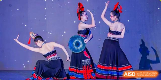 Two students from the Guangdong Overseas Chinese High School International Curriculum performing a traditional or cultural dance in dark costumes with fans.