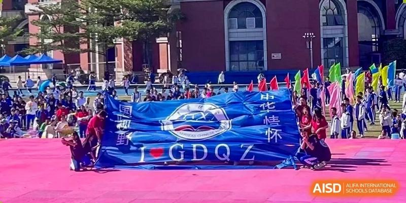 A large blue banner with white lettering displayed in the stands during an outdoor sporting event or competition for the Guangdong Overseas Chinese High School International Curriculum.