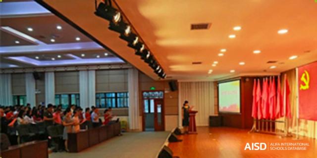 A speaker giving a lecture or presentation in a brightly lit indoor venue at the Guangdong Overseas Chinese High School International Curriculum.