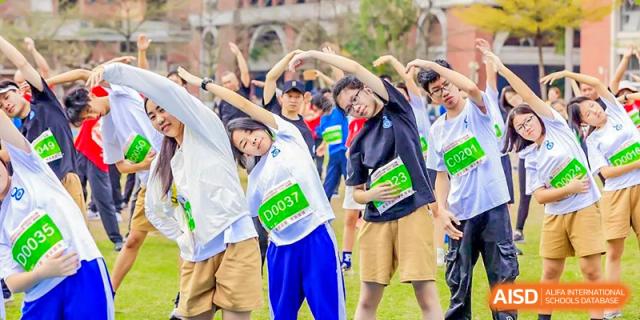 Guangdong Overseas Chinese High School International Curriculum students stretching and warming up in a group for a fitness or sports event.