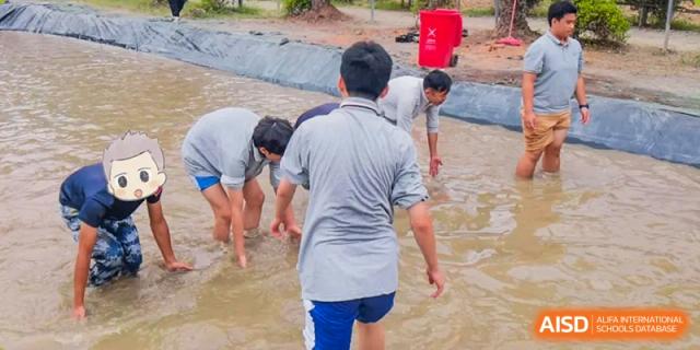 Guangdong Overseas Chinese High School International Curriculum students participating in a wet or muddy outdoor activity near a pool or trench.