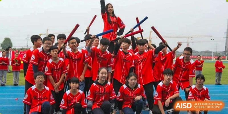 A large group of Wuhan Weiming Senior High School students wearing red sports jerseys and holding drumsticks or bats for a performance or cheering squad.