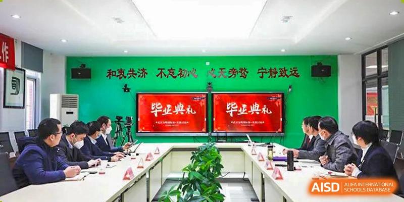An empty Wuhan Weiming Senior High School conference room or presentation hall with screens displaying the text "Graduation Ceremony" (or similar Chinese text).