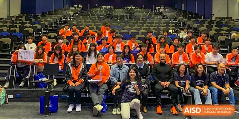 A group of Wuhan Weiming Senior High School students and teachers sitting together and posing for a photo in a large assembly hall or lecture theater.