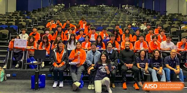A group of Wuhan Weiming Senior High School students and teachers sitting together and posing for a photo in a large assembly hall or lecture theater.