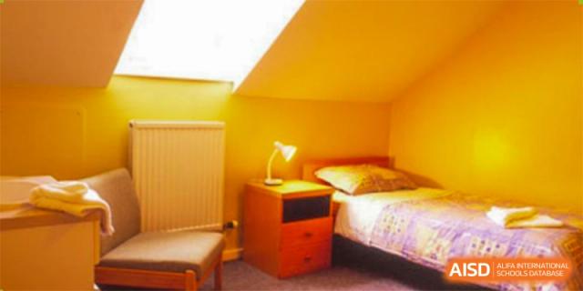 A cozy, older dormitory room at Wuhan Weiming Senior High School with a bed, nightstand, and lamp.