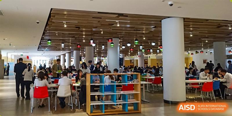 The bustling cafeteria or dining hall, showing many students and a book shelf/divider at Wuhan Weiming Senior High School.
