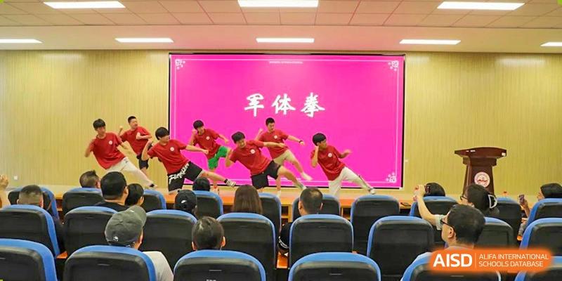 Wuhan Weiming Senior High School students in red shirts performing a martial arts routine on stage for an audience (Chinese text for 'Military Exercise' visible).