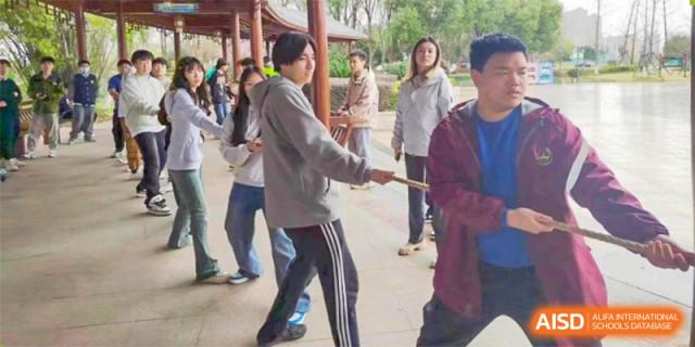 Two Wuhan Weiming Senior High School students competing in a stick or rope-pulling game during an outdoor event.