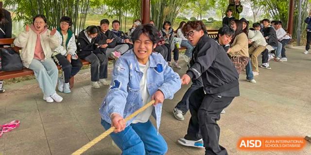 A happy Wuhan Weiming Senior High School student pulling on a rope during an outdoor tug-of-war game or sports day activity.