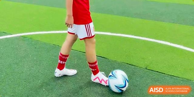 Close-up of a Wuhan Weiming Senior High School student's feet in white shorts and red socks dribbling a soccer ball on a green turf field.