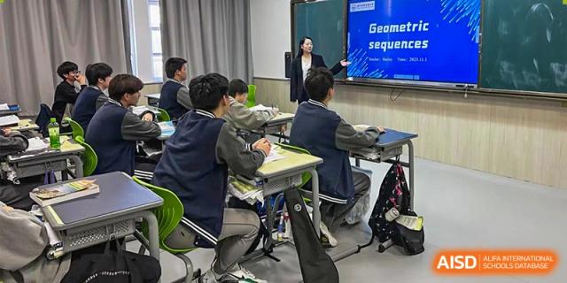 A Wuhan Weiming Senior High School class in session, with a teacher presenting information on a large digital screen to seated students.