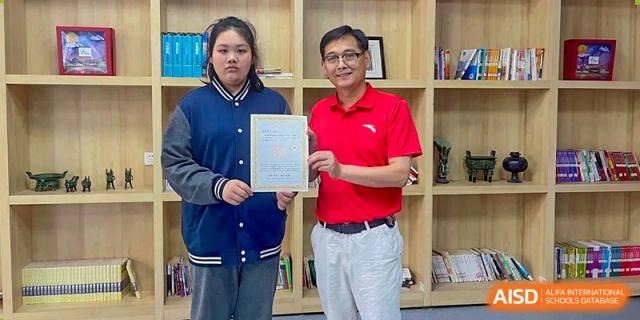 A Wuhan Weiming Senior High School teacher or principal presenting an award certificate to a student in the library.