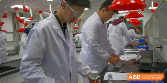Two Wuhan Weiming Senior High School students in lab coats and safety glasses conducting a science experiment or practical class.