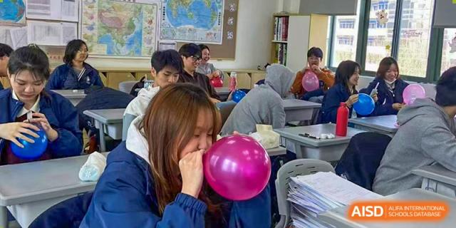Students in a classroom, with one female student blowing up a pink balloon at the Shanghai Jincai High School International Division.