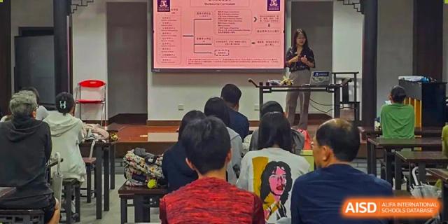 Students sitting in a lecture hall looking at a large screen with a teacher standing beside it at the Shanghai Jincai High School International Division.