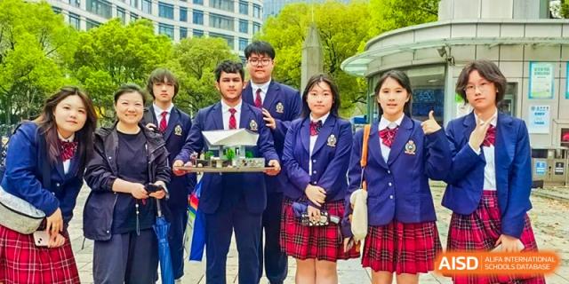 Four students in school uniforms holding up a science project or diorama at the Shanghai Jincai High School International Division.