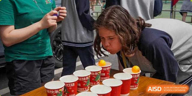 A student blowing a ping-pong ball across the tops of red cups as part of a game at the Shanghai Jincai High School International Division.