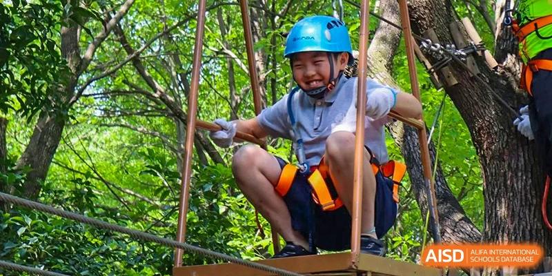 A student wearing a helmet and a safety harness, smiling while on a rope obstacle course at the Shanghai Jincai High School International Division.