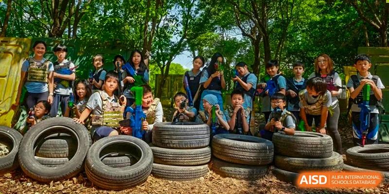Students with goggles and helmets posing in a fort made of old tires during an outdoor activity at the Shanghai Jincai High School International Division.