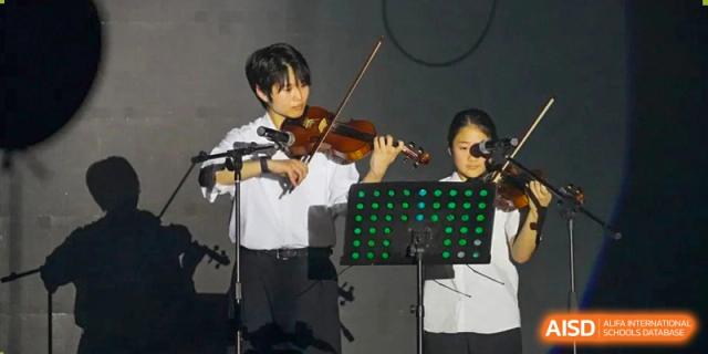 A male student playing the violin on a stage with other students and a music stand at the Shanghai Jincai High School International Division.
