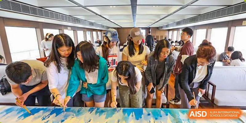 A group of students bending over to look at a large painting or creative project on the floor at the Shanghai Jincai High School International Division.