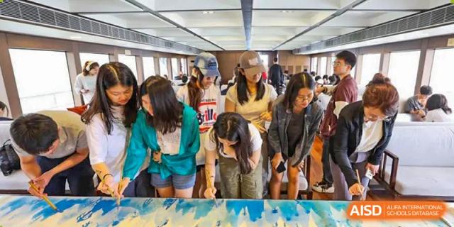 A group of students bending over to look at a large painting or creative project on the floor at the Shanghai Jincai High School International Division.