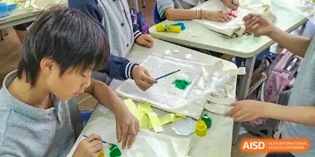Students hands painting with green watercolor on a canvas during an art class at the Shanghai Jincai High School International Division.