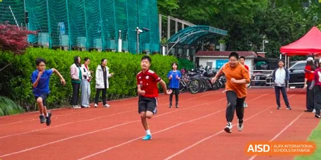 A male student in a red shirt running on a track during a race at the Shanghai Jincai High School International Division.