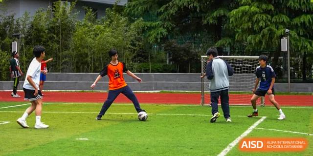 Two students playing soccer on a grass field at the Shanghai Jincai High School International Division.