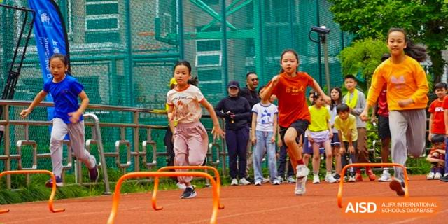 A female student jumping over a hurdle on a track while other students watch at the Shanghai Jincai High School International Division.