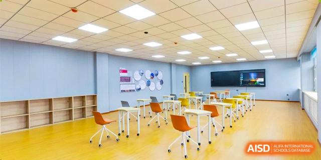 A brightly lit, modern classroom featuring individual orange and white desks and chairs on a yellow floor, ready for class. Canada British Colombia International Schools-Hefei.
