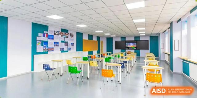 An empty, contemporary classroom with white, green, and orange desks arranged for group work, featuring unique ceiling and wall designs. Canada British Colombia International Schools-Hefei.