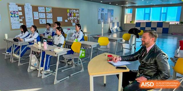 Students seated at individual desks in a colorful classroom, actively engaged in a lesson or group discussion. Canada British Colombia International Schools-Hefei.
