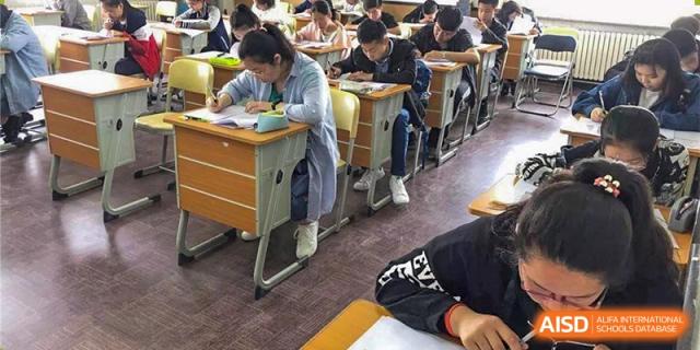 Students seated at desks taking a test or working on assignments in a busy classroom. Canada British Colombia International Schools-Hefei.