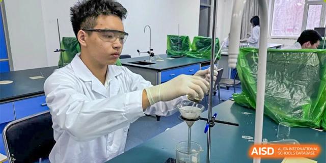 A male student in safety glasses and a lab coat performing a filtration experiment using laboratory glassware. Canada British Colombia International Schools-Hefei.