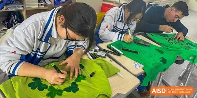A close-up of a female student in uniform decorating a green t-shirt with black markers as part of a creative or art class project. Canada British Colombia International Schools-Hefei.